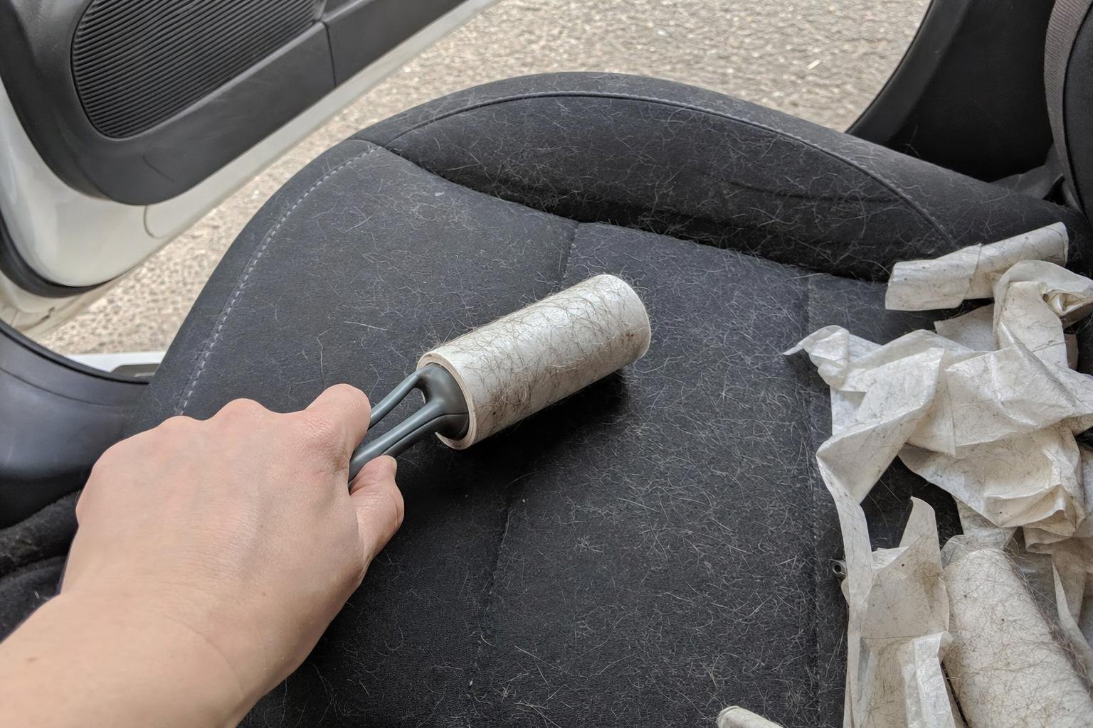 A hand using a clogged lint roller on a hairy car seat